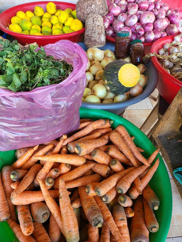 A vibrant selection of fresh vegetables and herbs at a local market, showcasing carrots, lemons, onions, and greens.